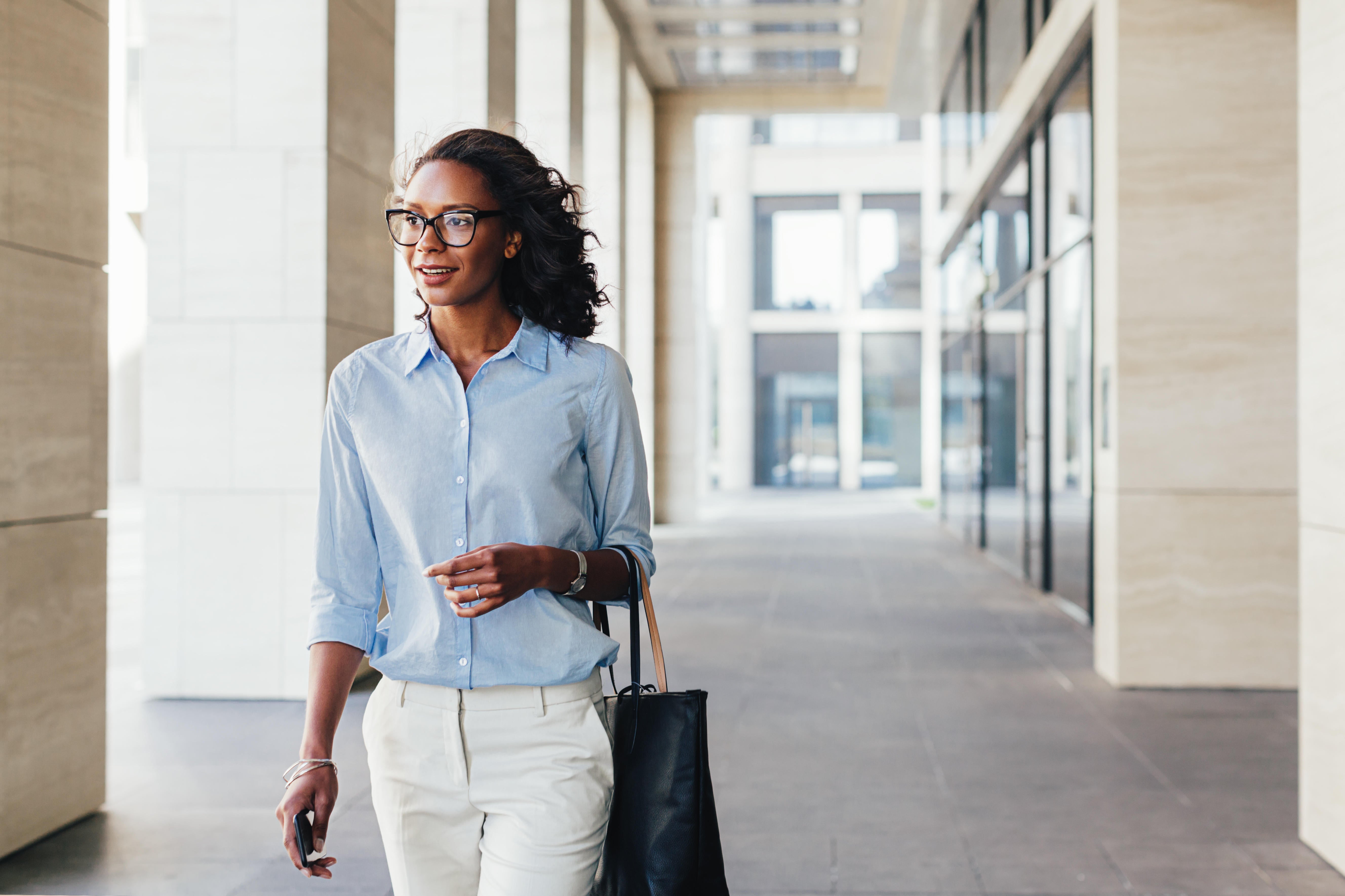 Female business professional walking outside an office building with bag on a hand 