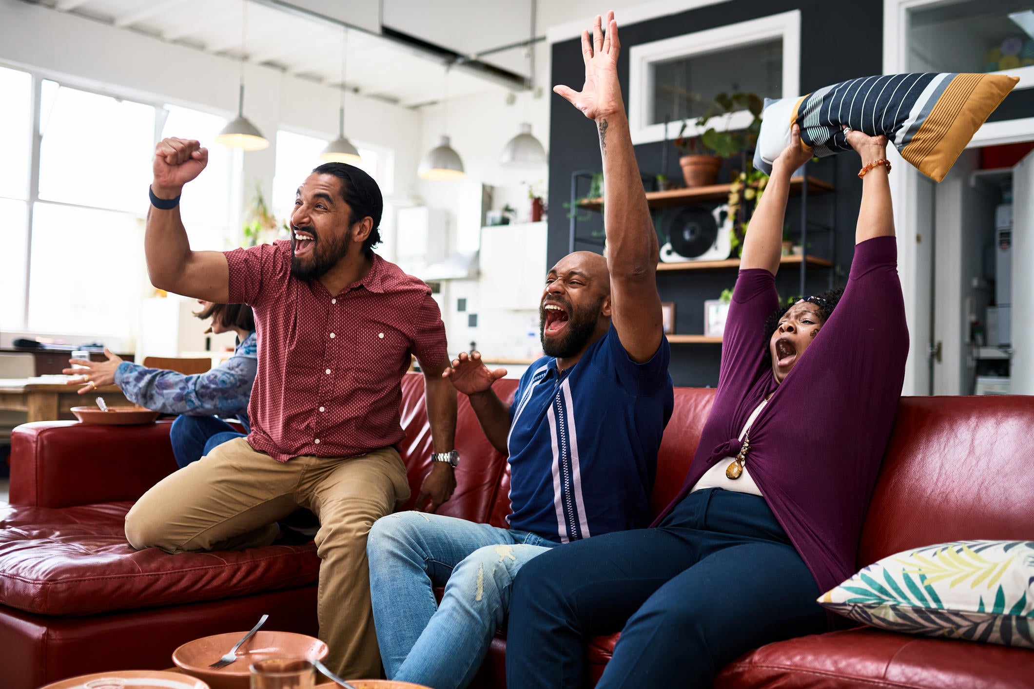 Friends watching TV at home and cheering with arms raised 