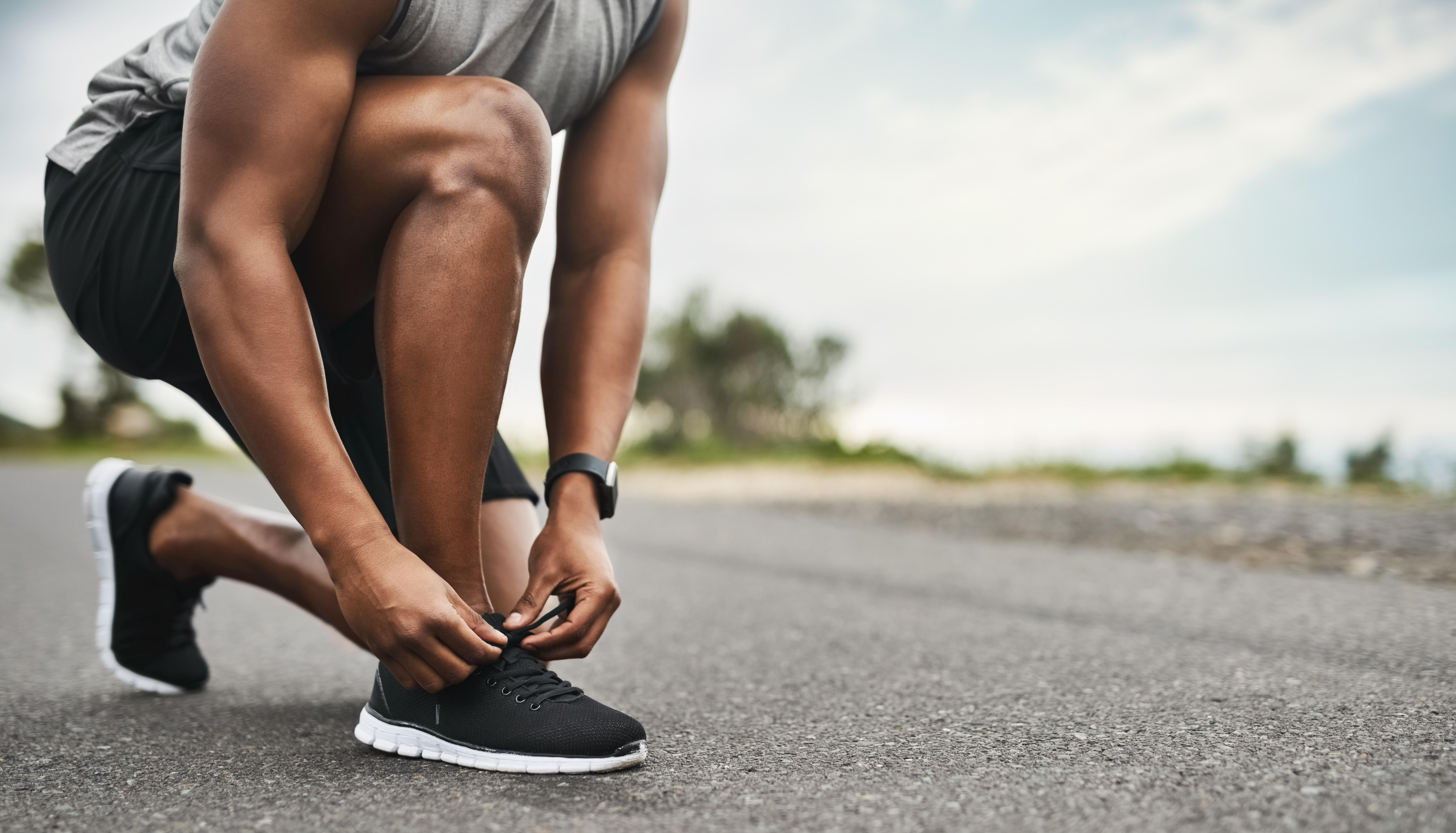 Man kneeling down to tie a black running shoe 