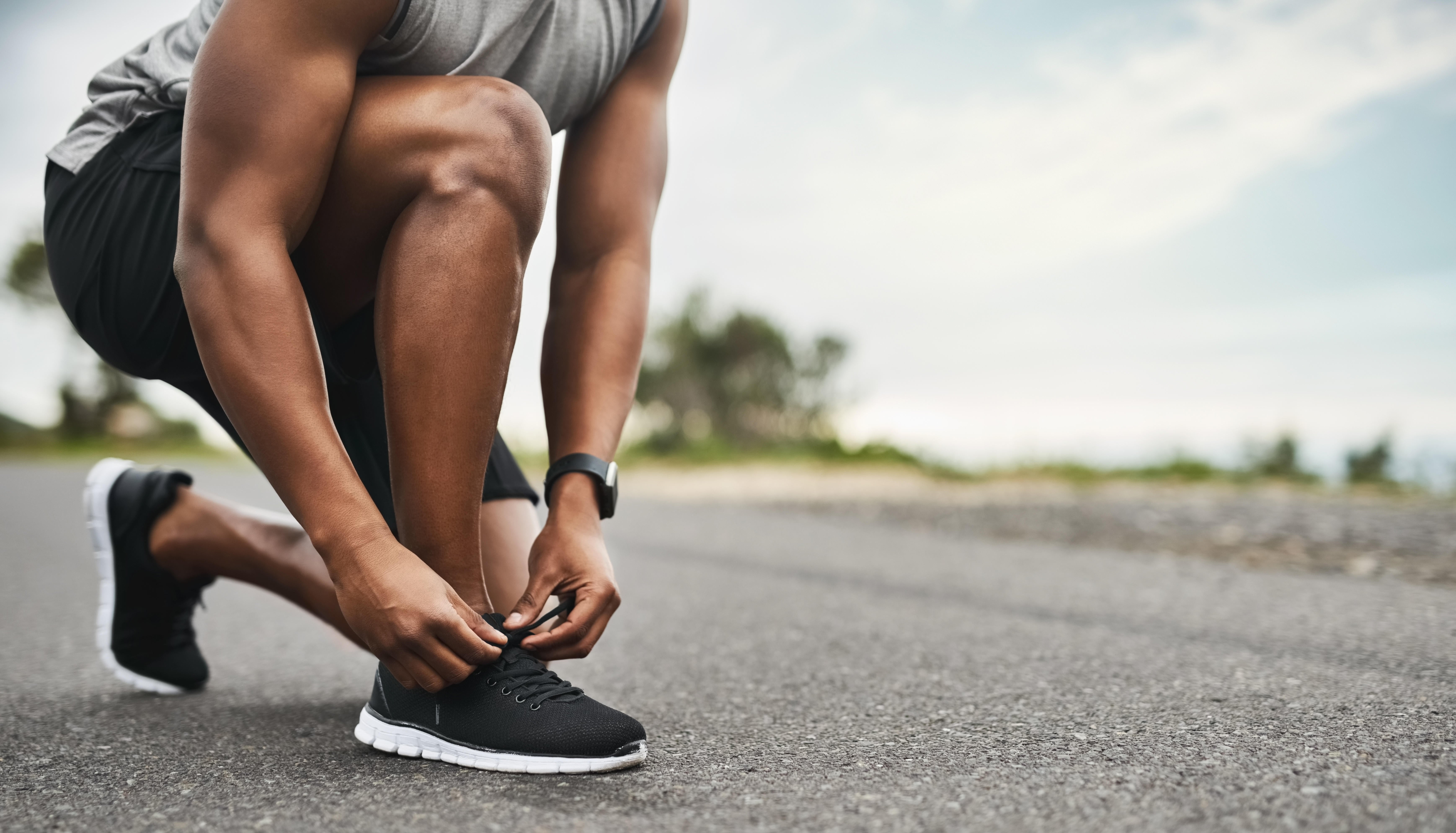 Man kneeling down to tie a black running shoe