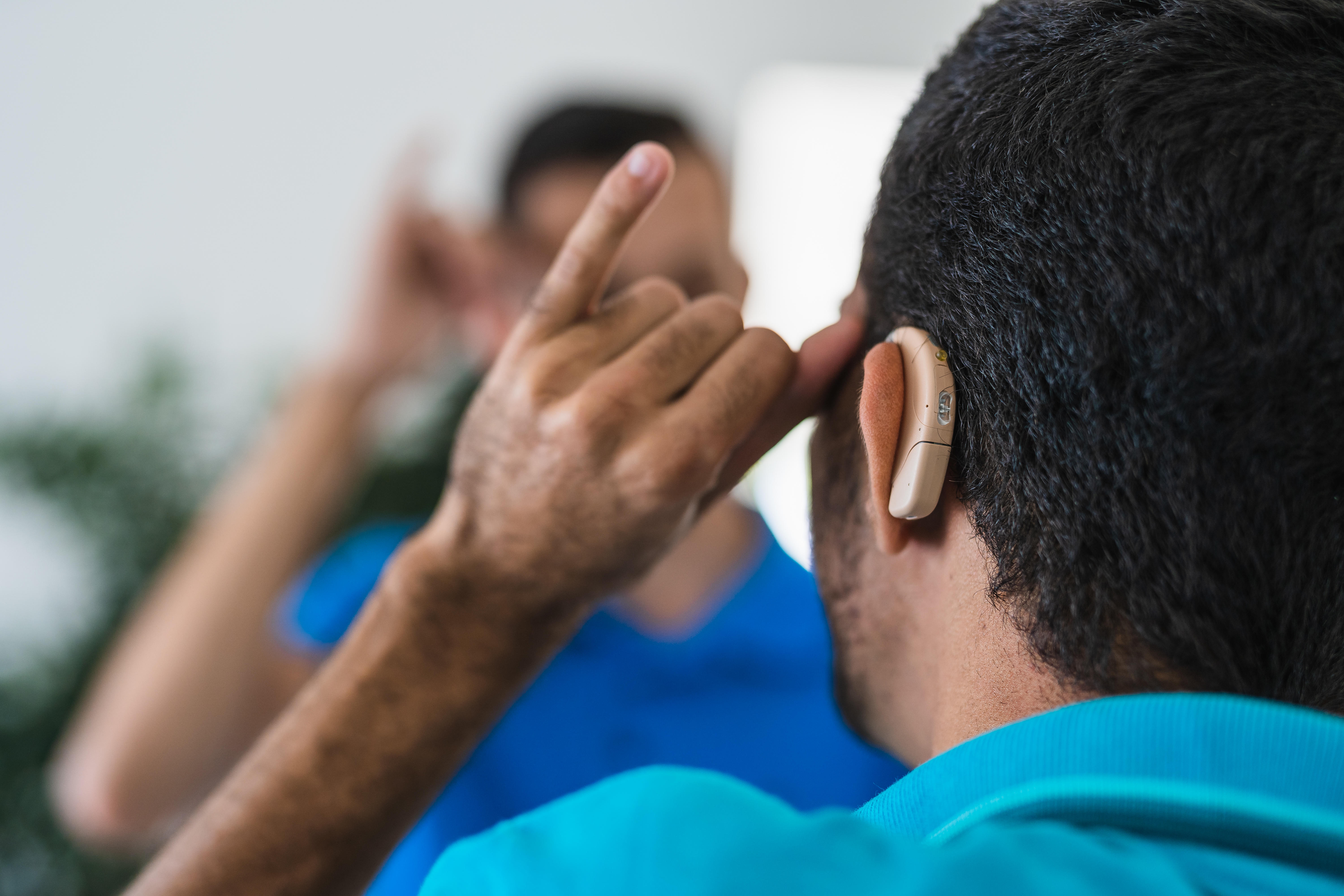 A person adjusts their behind-the-ear hearing aid while looking in the mirror. 