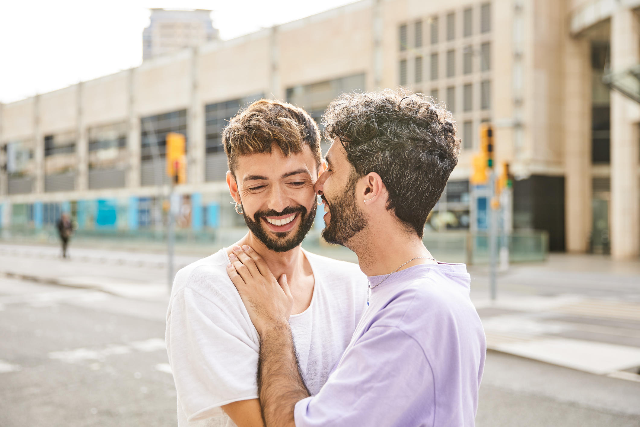 A gay couple share smiles and an intimate moment on a city street. 