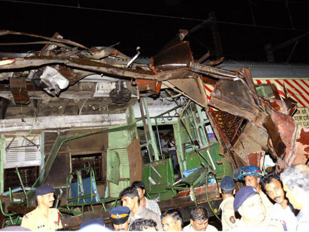 Police and onlookers stand around the mangled compartment of one of the blast affected local trains in Mumbai 