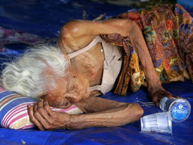 elderly Indonesian woman lies on the floor of a tent 