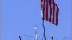 A U.S. soldier is seen behind barbed wire, next to the American flag on the roof of the U.S. Embassy in Damascus, Syria 