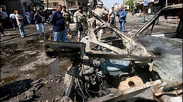 Iraqi and US troops stand near the wreckage of car bomb near the Abu Tibeekh restaurant in Sadoun Street in central Baghdad 