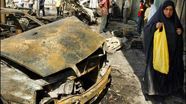 An Iraqi woman walks past the wreckage of a car at the site where a carbomb exploded at Baghdad's al-Bayaa neighborhood 