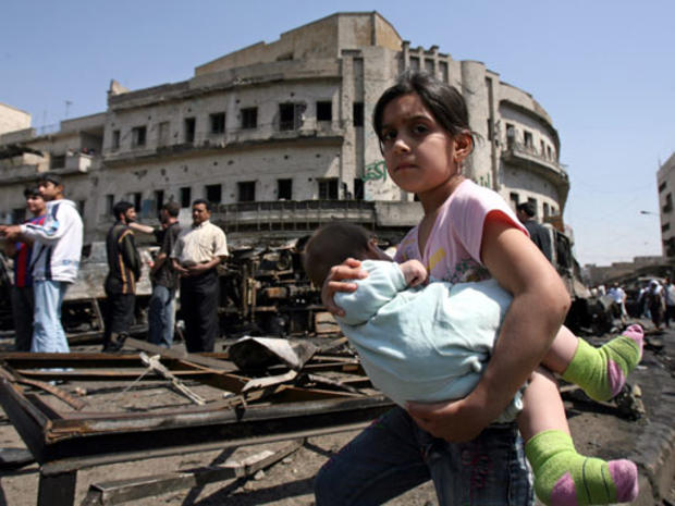 A girl carries a baby past the scene of the previous days car bomb attack that killed least 127 people and injured 148 at the Sadriyah market in Baghdad, Iraq, Thursday, April 19, 2007. 