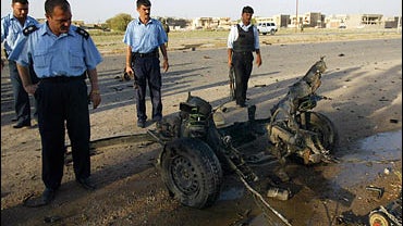 Iraqi policemen inspect the wreckage of a car 