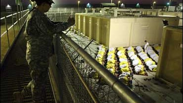 A military policewoman looks over Iraqi detainees praying at Camp Cropper, Baghdad 