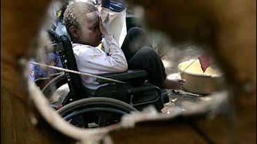 An internally displaced child sitting on a wheelchair is framed through a gap in a tent in an IDP camp 