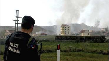 A police officer stands guard as smoke billows at the site of a powerful explosion at an army depot in Gerdec, ALbania 