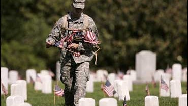 A soldier canvases Arlington National Cemetery placing American flags at headstones 