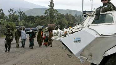 A Congolese soldier and displaced people pass a United Nations armoured vehicle in Goma 