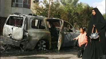 An Iraqi woman walks with her child next to a damaged car after a bomb explosion in the Mashtal neighborhood of eastern Baghdad 