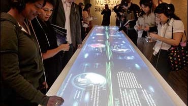 Erica Carter, 32, left, and Mar Fujimoto, 29, second from left, view "The Crossroads Table," an interactive exhibit that draws attention to 160 genres of music and how they relate to one another, at the Grammy Museum Tuesday, Dec. 2, 2008, in Los Angeles. 