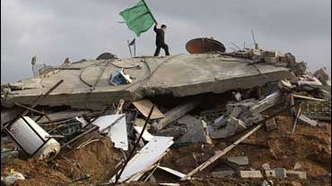 A Palestinian boy holds a Hamas flag over a destroyed house in Beit Lahia 