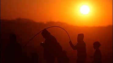 A Palestinian man and youths are seen in a field, as the sun sets on the outskirts of the West Bank city of Ramallah, Wednesday, Jan. 21, 2009. 