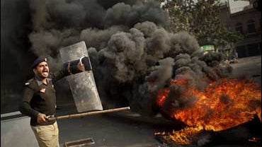 A Pakistani police officer reacts next to burning tires during clashes in Lahore, Pakistan 