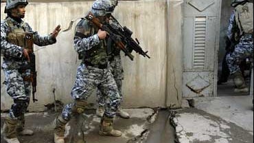 In this March 16, 2009 file photo, a U.S. Army soldier stands guard as Iraqi police officers enter a house during a joint search operation in southwestern Mosul, 225 miles northwest of Baghdad, Iraq. 