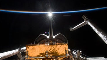 Space Shuttle Atlantis is backdropped by the blackness of space and the thin line of Earth's atmosphere 