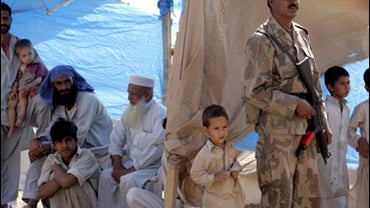 A Pakistani army soldier stands guard as displaced people watch a helicopter carrying top U.S. envoy to Pakistan and Afghanistan Richard Holbrooke, unseen, lands at the Chota Lahore refugee camp, at Swabi 