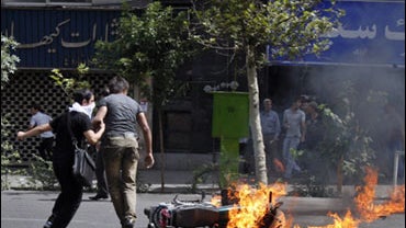 Iranian protesters walk past a burning motorcycle in Tehran, Iran, Sunday, June 14, 2009. 