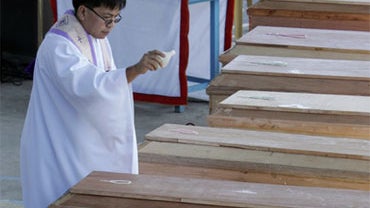 A Filipino priest sprinkles holy water on wooden coffins of a family of eight during a mass burial for landslide victims in Baguio city, northern Philippines on Monday Oct. 12, 2009. 