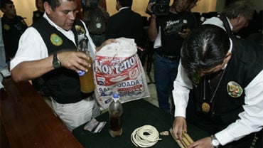 A police officer displays two bottles containing human fat while another sets seized sticks of dynamite during a press conference in Lima, Thursday, Nov. 19, 2009. 