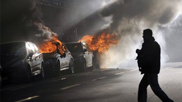 A photographer walks towards burning cars during a protest against the seventh WTO Ministerial Conference in the streets of Geneva, Switzerland, Saturday, Nov. 28, 2009. 