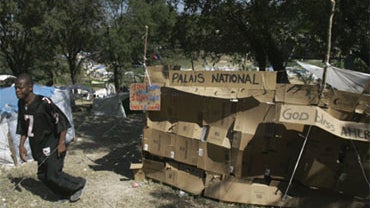 A man walks by a tent made of cardboard boxes with the sign "National Palace" in the Delmas 40 refugee camp for earthquake survivors in Port-au-Prince, Friday, Jan. 22, 2010. 