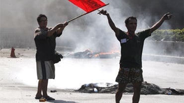 An anti-government protester wavea a flag after setting fire on tires on Saturday, May 15, 2010 in Bangkok, Thailand. 