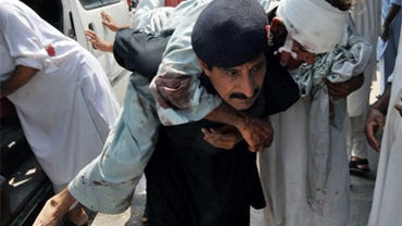 A Pakistani security guard helps an injured blast victim as he arrives at a hospital in Peshawar on July 9, 2010, following a suicide bomb attack in district of Mohmand. 