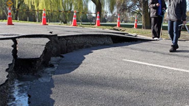 Locals look at a seismic rupture in a road in Christchurch on September 4, 2010 after a powerful earthquake.  