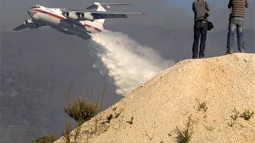 Photographers take pictures as an Ilyushin-76 tanker plane sprays its load of water over flames in the Carmel Forest in the outskirts of Haifa on December 4, 2010 as thousands of Israeli firemen and rescuers fight to control the massive forest fire that h 