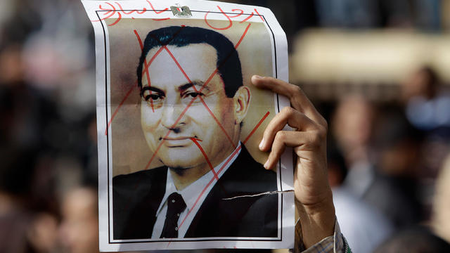 An Egyptian anti-government protester holds a defaced poster of Egyptian President Hosni Mubarak, 