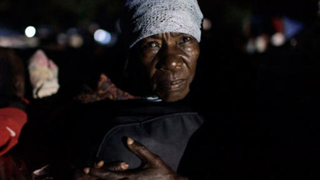 woman holds tight to her belongings while spending the night at a makeshift camp 