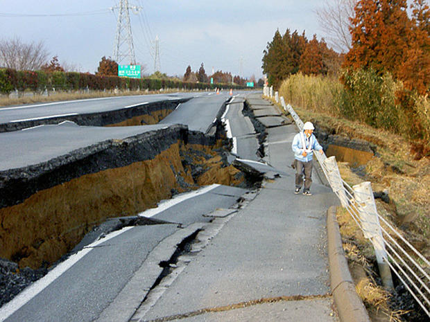 After earthquake in japan, worker examines road. 