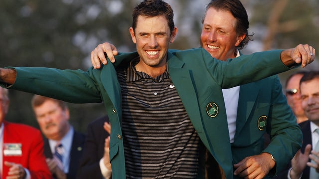 Former champion Phil Mickelson, back, helps Charl Schwartzel of South Africa with his green Masters jacket 