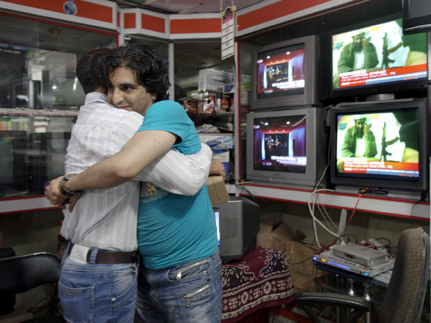 Afghan men working at a TV shop hug each other while watching the news of the death of Osama bin Laden  