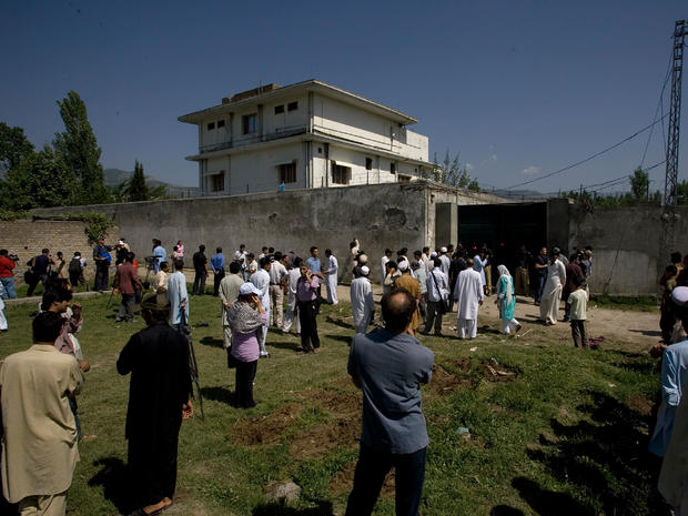 Locals gather outside the perimeter wall and sealed gate into the compound and a house where Osama bin Laden was caught and killed 