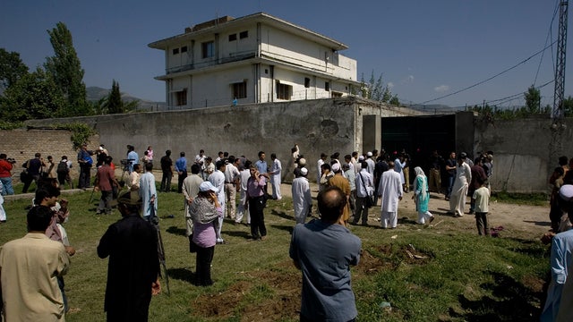 Locals gather outside the perimeter wall and sealed gate into the compound and a house where Osama bin Laden was caught and killed 
