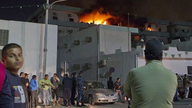  In this photo taken on a government organized tour, soldiers and civilians gather in front of a burning official building following an airstrike in Tripoli, Libya, May 17, 2011.  