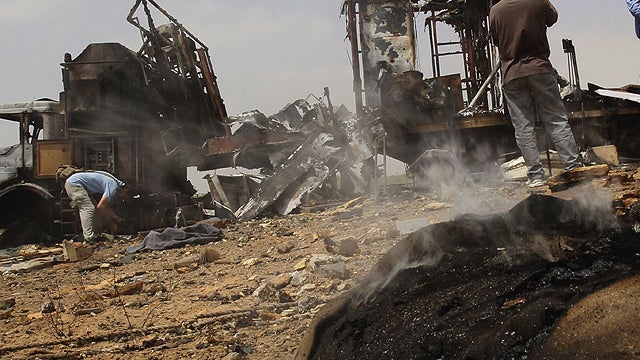 In this photo taken on a organized government tour smoke rises from debris as foreign journalists take photographs next to a damaged truck at the Hadba agricultural area, outside Tripoli, Libya, on June 8, 2011, which Libyan officials claim was a target o 