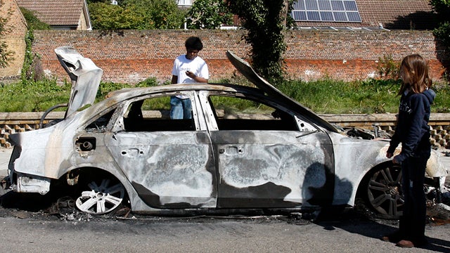 Local residents look at the shell of a burnt-out car in Enfield, London, Aug. 8, 2011. New unrest erupted in various locations in London Aug. 7, 2011, one day after rioting and looting took place in a deprived area prompted by community anger over a dispu 