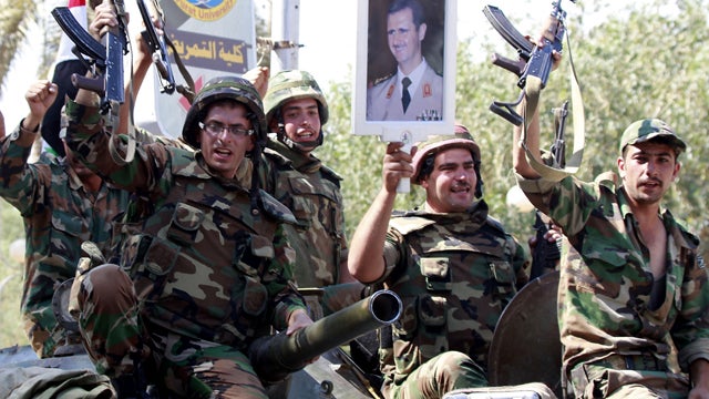 In this picture taken on a government-organized tour, Syrian soldiers raise their weapons while holding a picture of Syrian President Bashar Assad as they leave the eastern city of Deir Zor following a 10-day military operation Aug. 16, 2011. Syria has re 