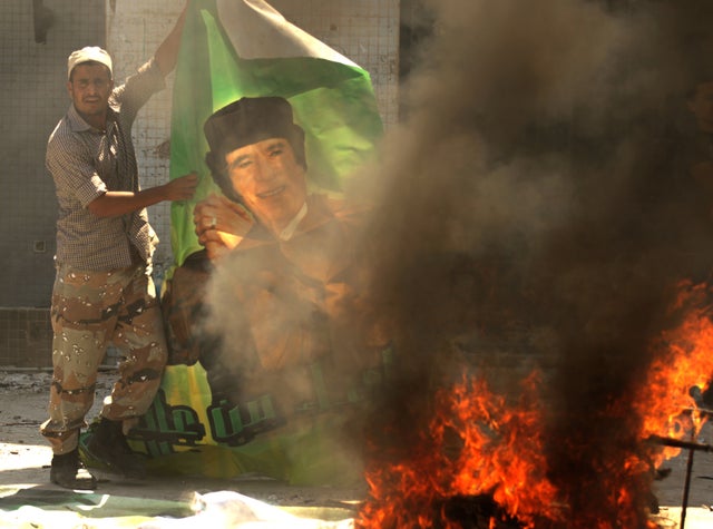 A Libyan rebel burns a poster of Moamer Kadhafi 