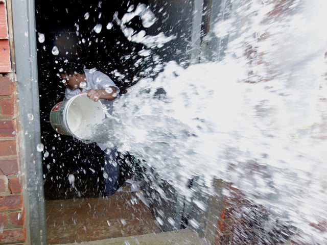 Melvin Flores uses a pail to scoop floodwaters out of his utility roo 