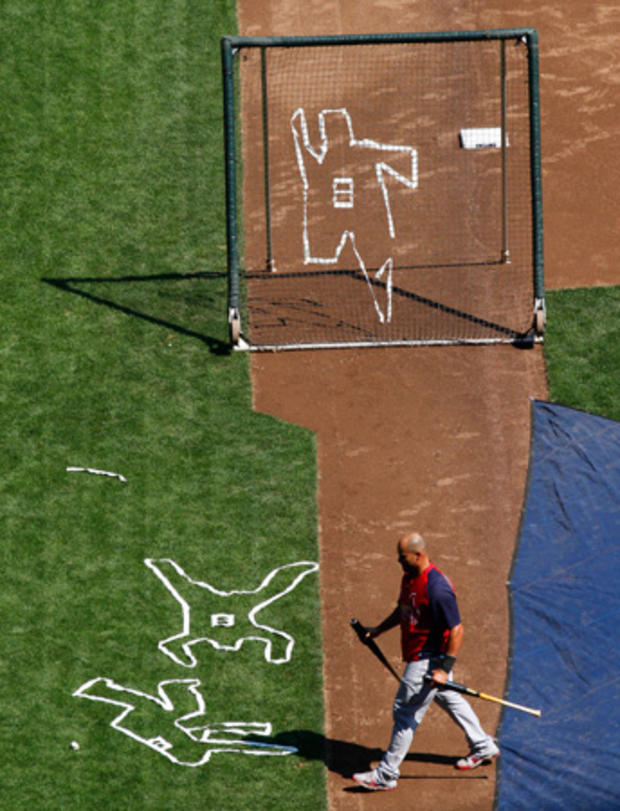 Albert Pujols walks past outlines depicting Milwaukee Brewers' Ryan Braun falling down 