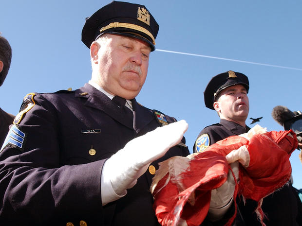 New York City Police Sgt. Joe Keenan, left, dusts off one of the three U.S. flags that have been recovered from ground zero during a presentation at the Golden Gate Bridge March 18, 2002, in San Francisco. Keenan brought the flag to San Francisco as a sho 